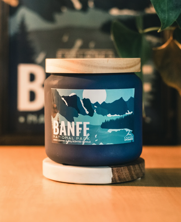 A large candle in a mason jar with a Banff National Park themed graphic on the front. By Canada Untamed on Etsy.