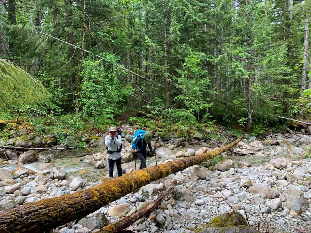 Two hikers crossing an unbridged creek on the Della Falls Trail