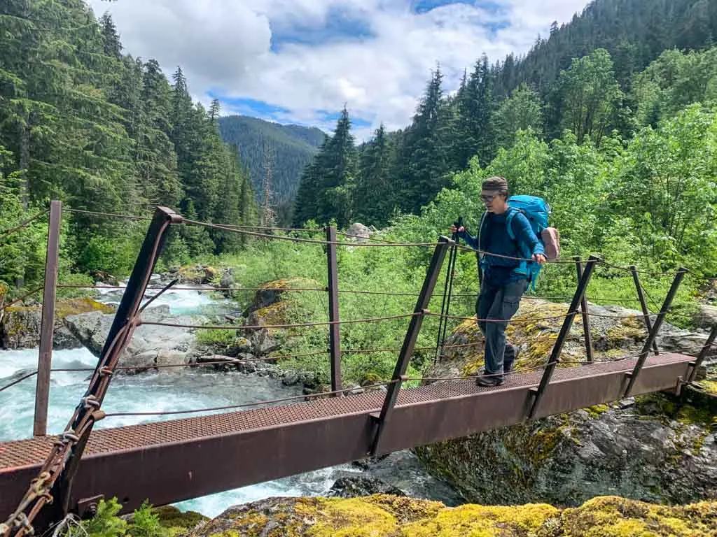 A hiker crosses a metal bridge over Drinkwater Creek