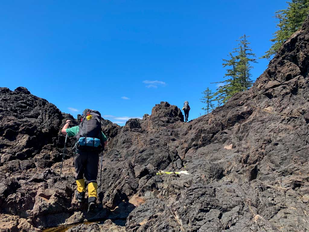 Two hikers scrambling across volcanic rocks at Mushroom Point