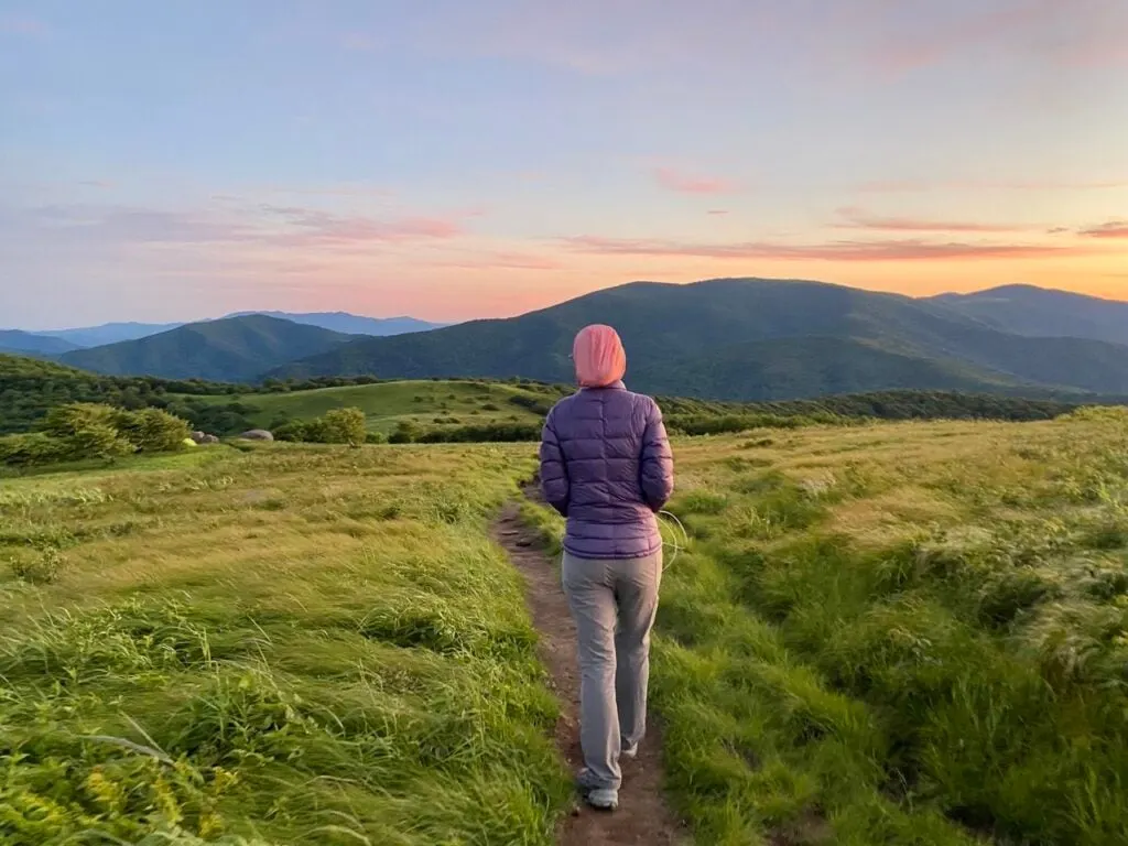 A woman wearing a puffy jacket, a pink knit hat, and Outdoor Research Ferrosi pants walks on a trail on top of a mountain on the Appalachian Trail