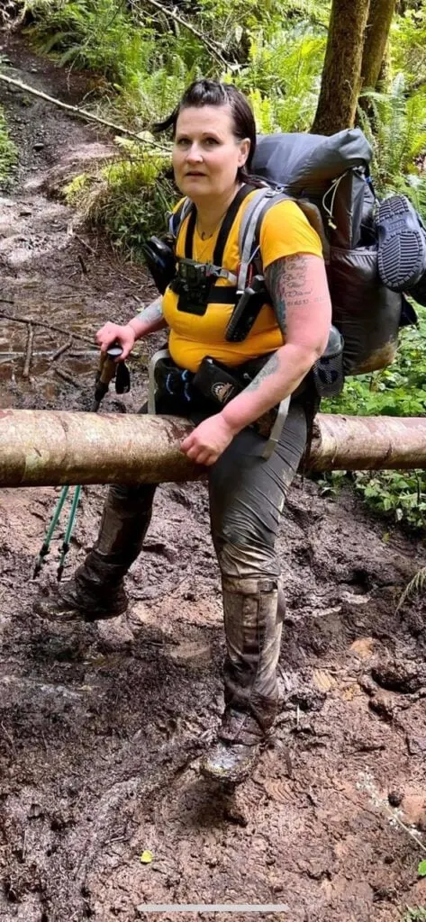 A woman wearing a yellow shirt and Arc'Teryx Gamma LT pants climbs over a log on a muddy trail