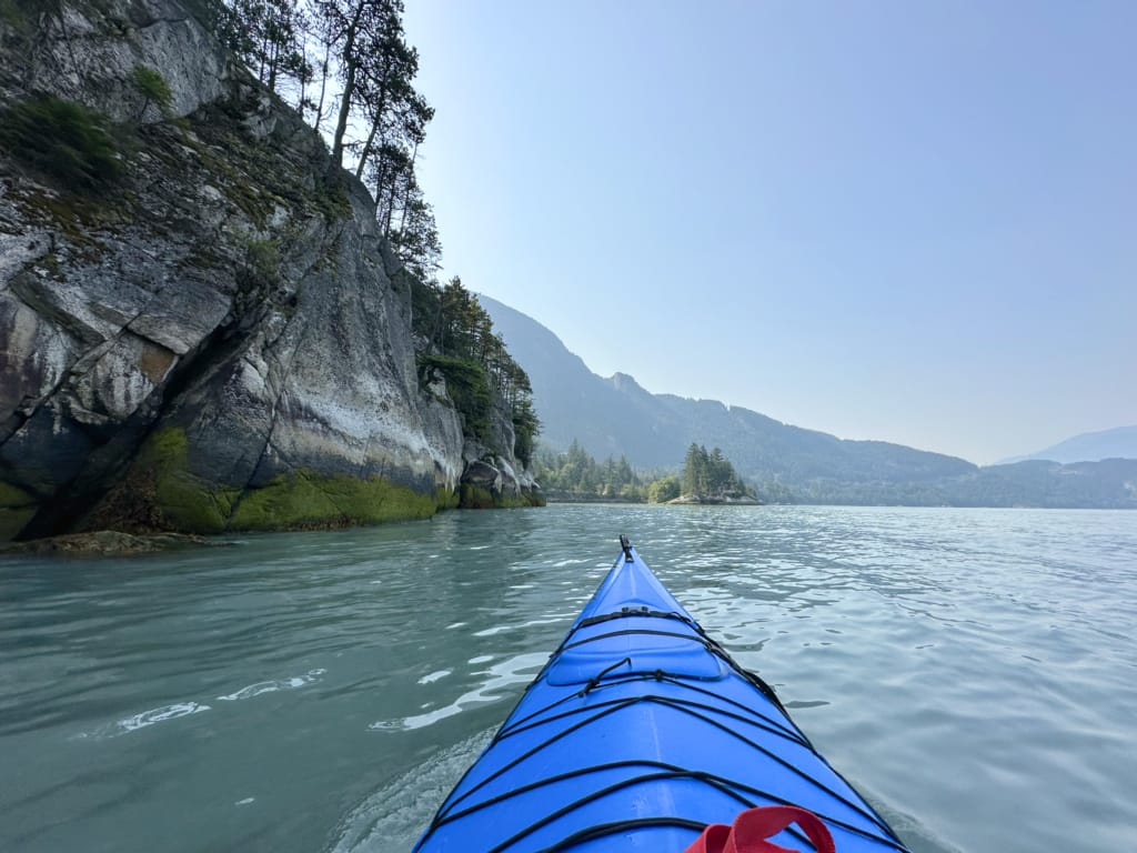 A kayker paddles past a granite cliff in Howe Sound near Squamish