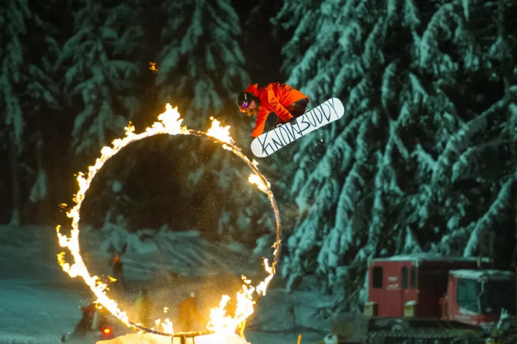 A snowboarder jumps through a flaming hoop.