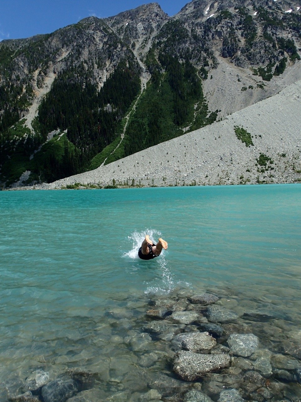 A hiker dives into a turquoise mountain lake