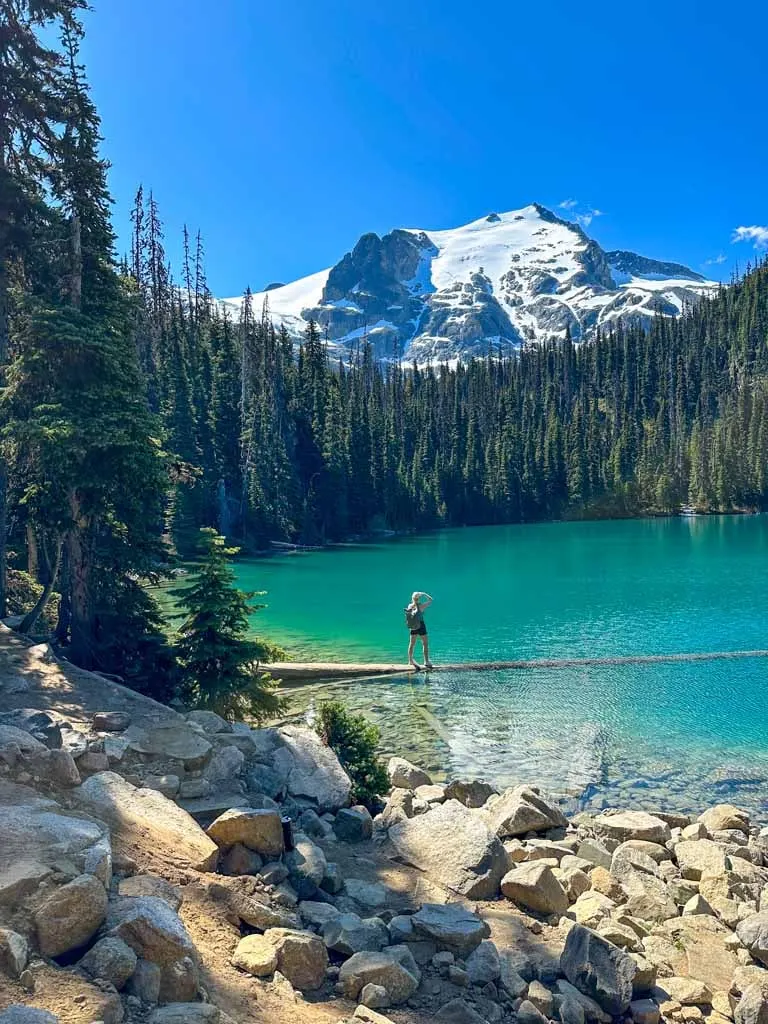 A hiker stands on the floating log in Middle Joffre Lake