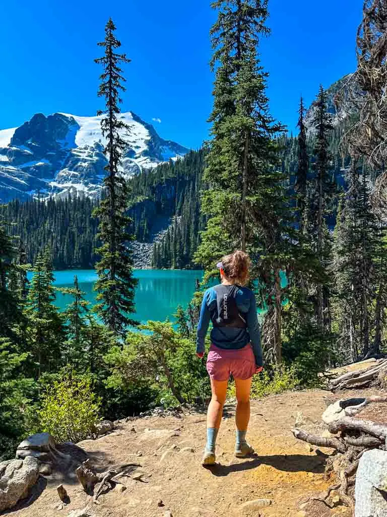 A woman hikes past a turquoise mountain lake