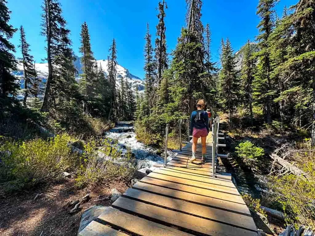 A hiker walks across a bridge on the Joffre Lakes hike