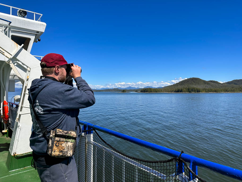 A man looks through binoculars on the ferry to Haida Gwaii