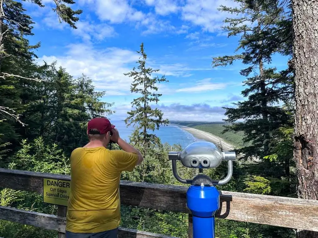 A person looks through binoculars at Tow Hill on Haida Gwaii. They are looking at North Beach and Rose Spit.