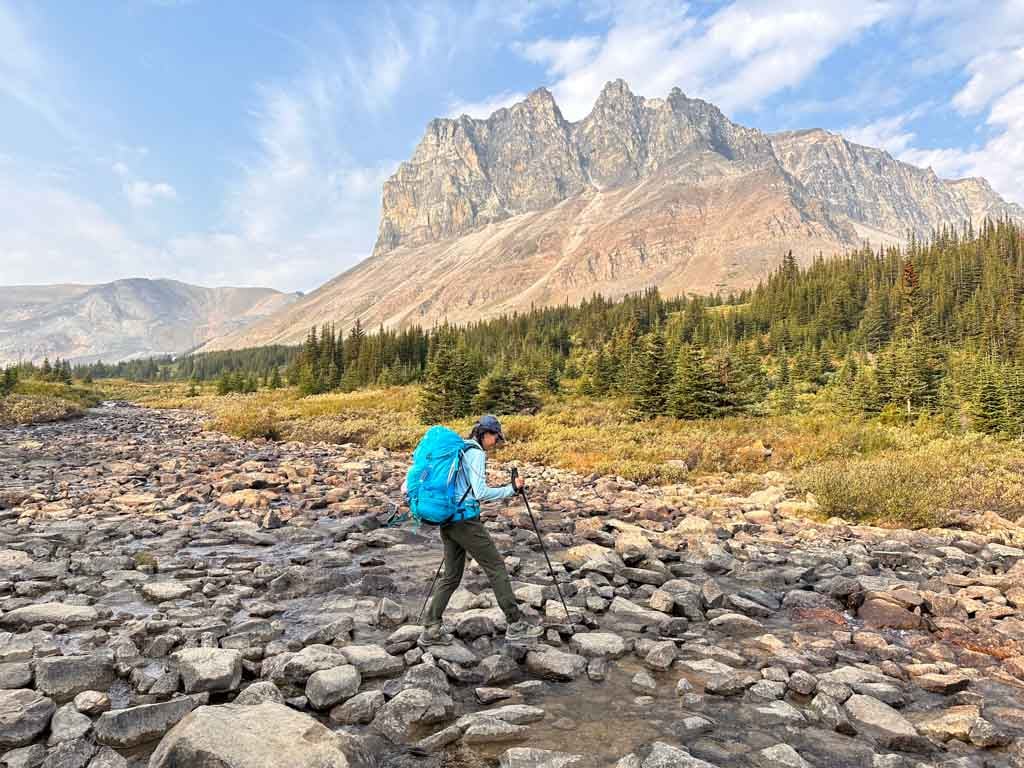 A woman crosses a creek in front of Tekarra Camp on the Skyline Trail - one of the best backpacking trips in the Canadian Rockies