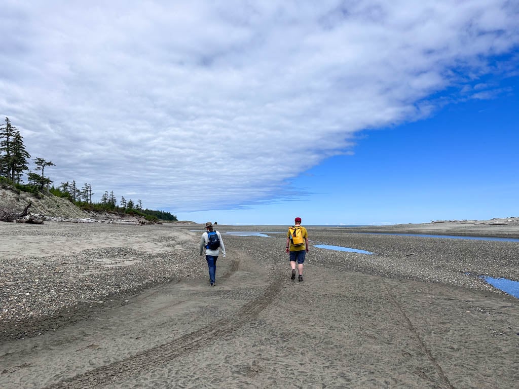 Two hikers walk along a beach next to the Tlell River in Naikoon Provincial Park