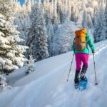 A woman snowshoes up a hill in a snowy forest - get suggestions for the best gifts for snowshoers