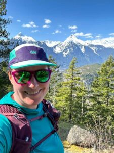 A woman wearing a Ciele trail running cap takes a selfie in the mountains
