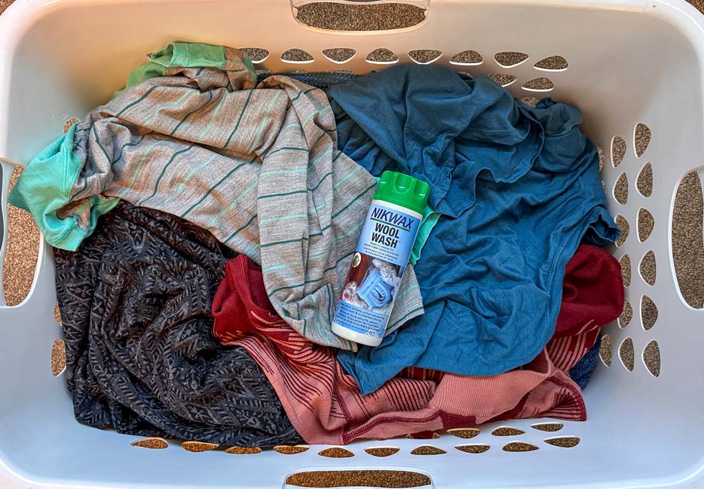 A laundry hamper of Merino wool hiking clothing with a bottle of Nikwax Wool Wash