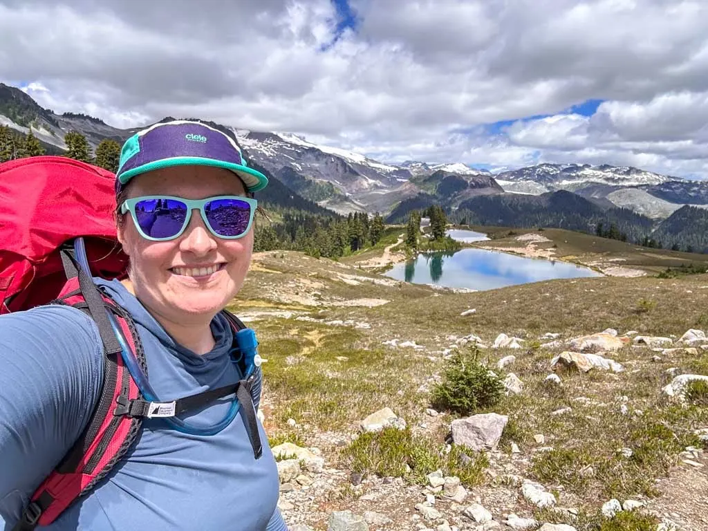 A hiker wearing an overnight pack takes a selfie in front of Elfin Lakes
