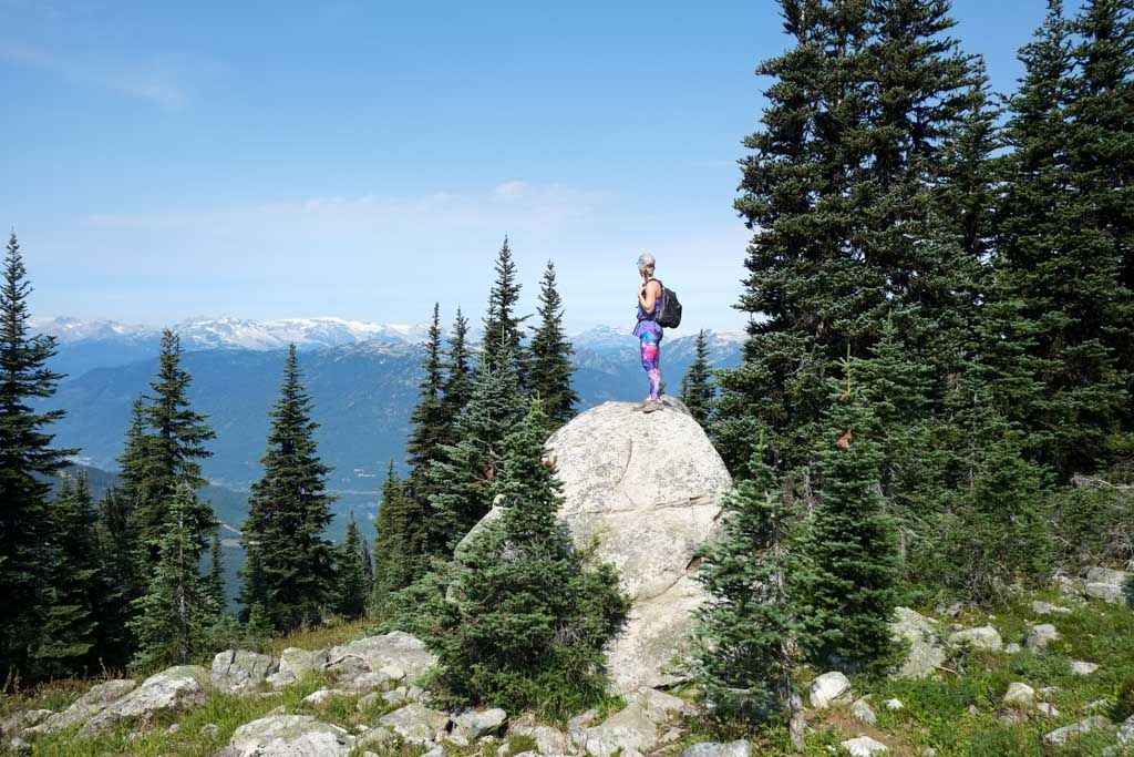 A woman stands on a rock to look at the views of the mountains in Whistler