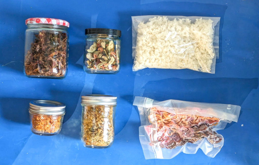 Four glass jars and two vacuum sealed bags of home dehydrated backpacking food