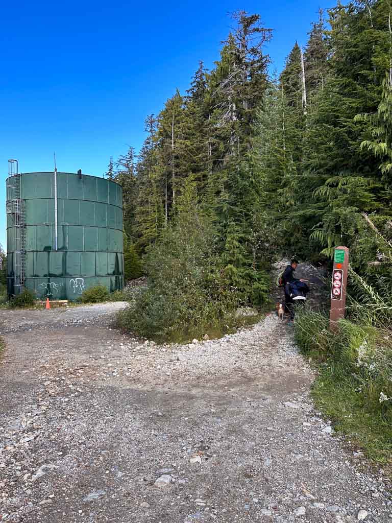 A giant green water tower next to a trail sign on the Howe Sound Creat Trail.