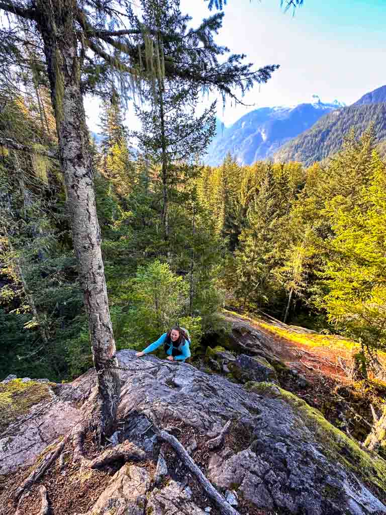 A woman uses a fixed rope to climb up a rocky bluff on a trail in Squamish