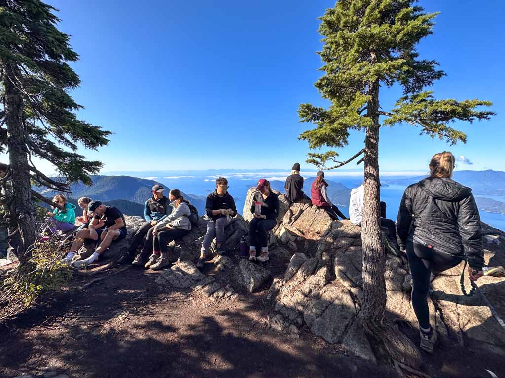 Eleven hikers sitting on a rock and blocking the viewpoint at St. Mark's Summit