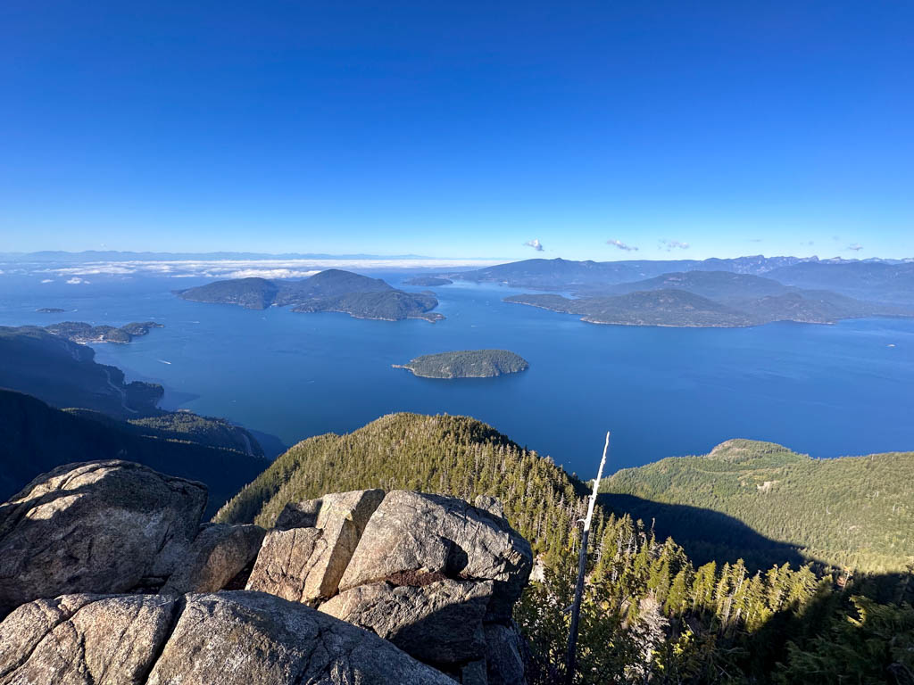 View of Howe Sound and islands from St. Mark's Summit. There are rocky cliffs and forest in the foreground. 