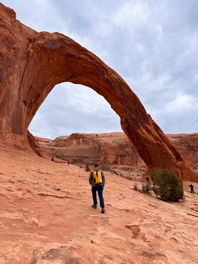 A hiker walks towards Corona Arch across red slickrock