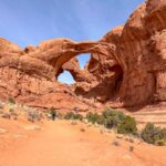 A trail with hikers leads to Double Arch in Arches National Park. Get tips for hiking in hot weather