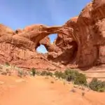 A trail with hikers leads to Double Arch in Arches National Park. Get tips for hiking in hot weather