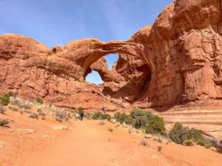 A trail with hikers leads to Double Arch in Arches National Park. Get tips for hiking in hot weather