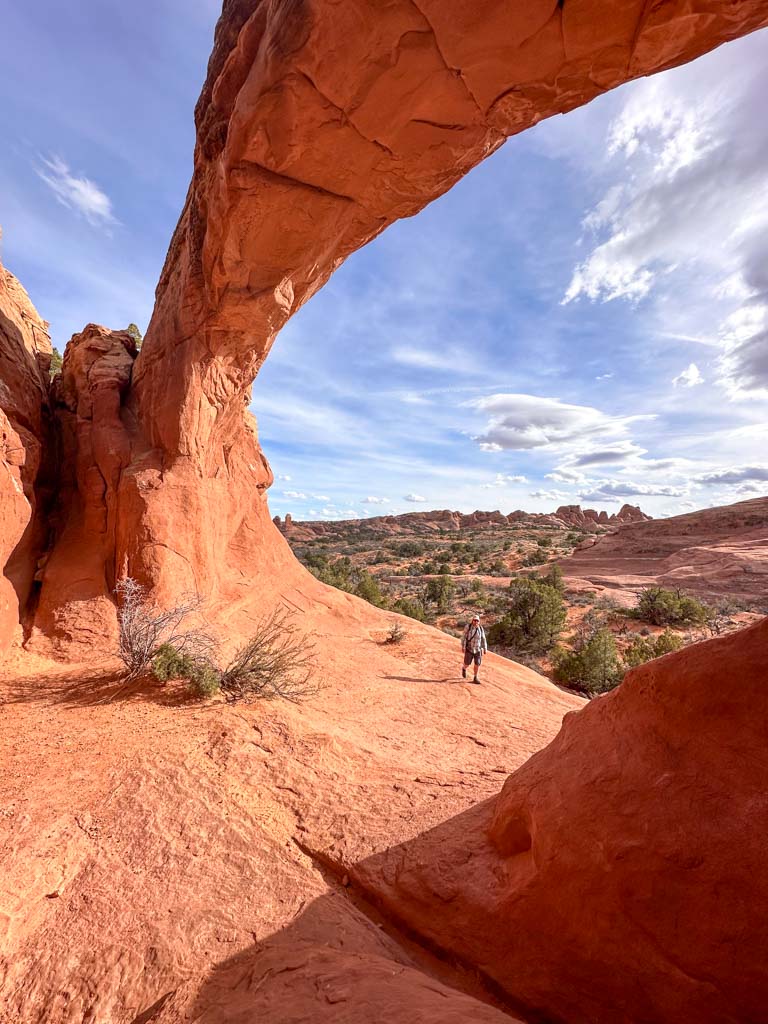 A hiker walks under Tapestry Arch in Arches National Park