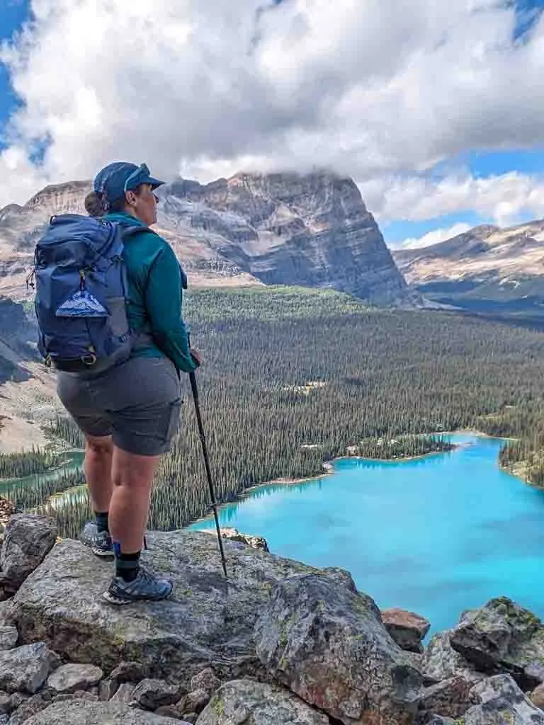 A hiker poses on a rock ledge at Lake O'Hara wearing the Outdoor Research Echo Hoodie