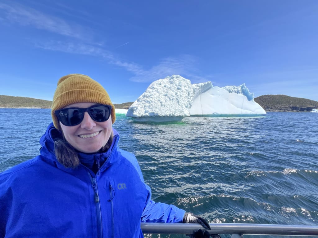 A woman poses with an iceberg on a boat tour in Twillingate