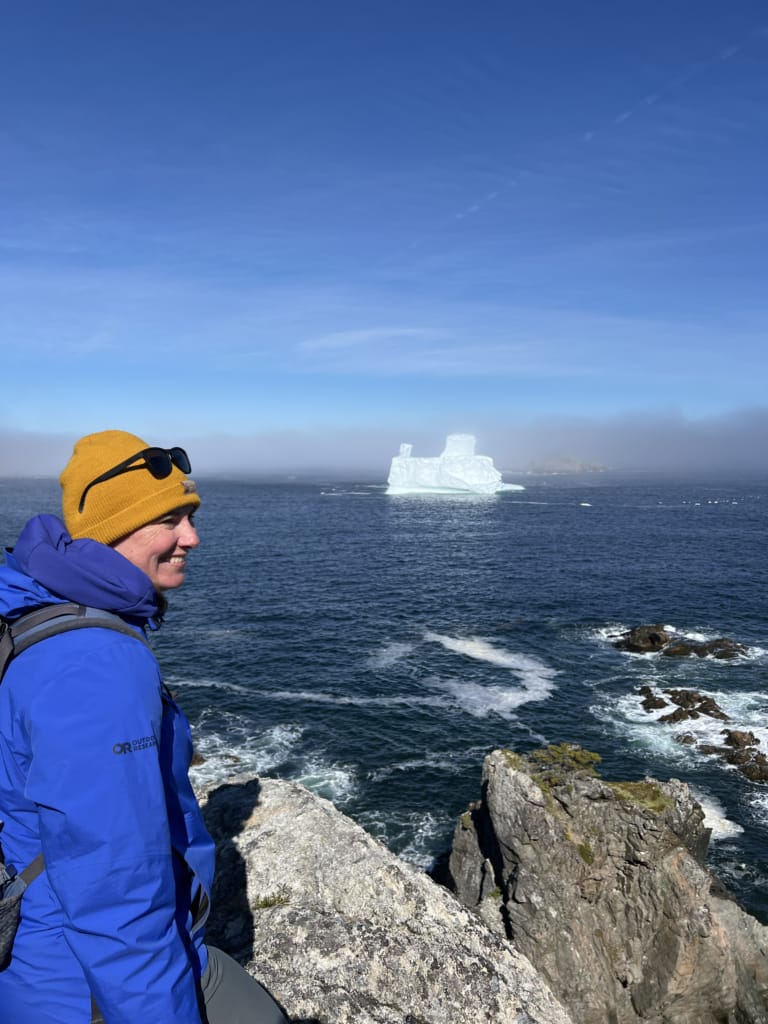 A hiker on the Little Harbour Trail in Twillingate with an iceberg in the background