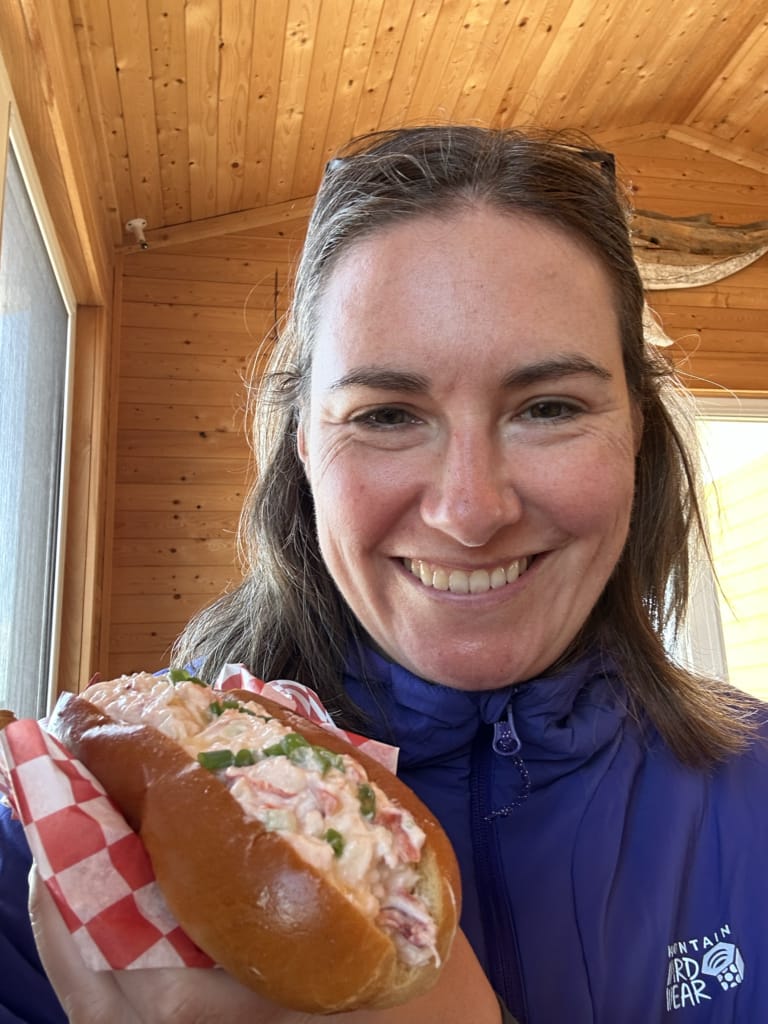 A woman holds a lobster roll close to the camera