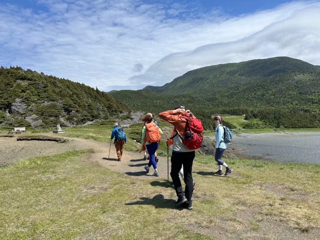 A group of hikers bundled up against the wind on a sunny day at Bottle Cove