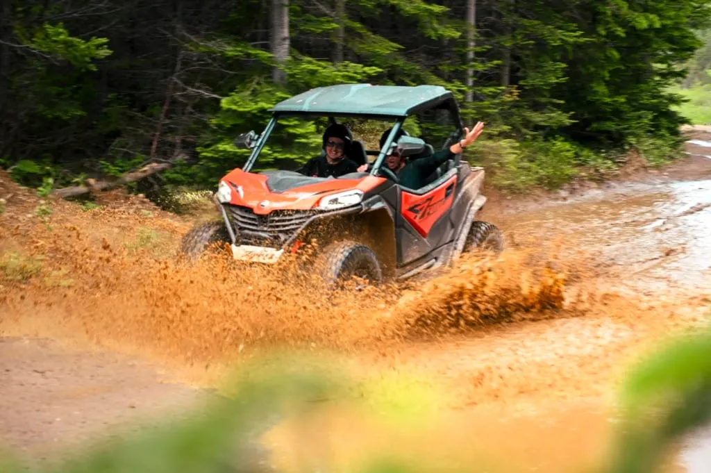 Two people drive a side-by-side ATV through a mud puddle