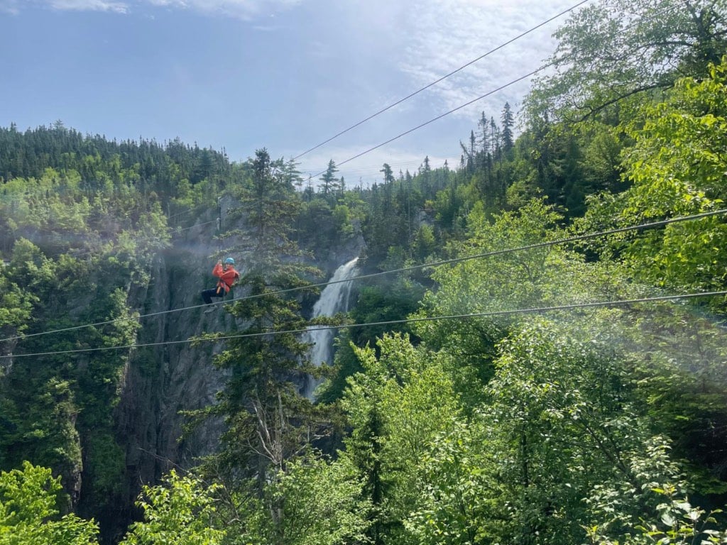 A woman rides a zipline in front of Steady Brook Falls at Marble Mountain in Newfoundland