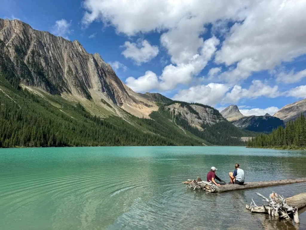 Two hikers sit on a log at Sherbrooke Lake in the Canadian Rockies