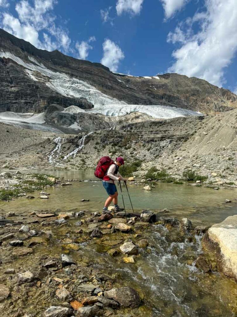 A hiker rock hops across a creek on the Iceline Trail