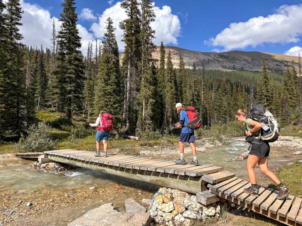 Hikers cross the bridge over the Little Yoho River near the Stanley Mitchell Hut