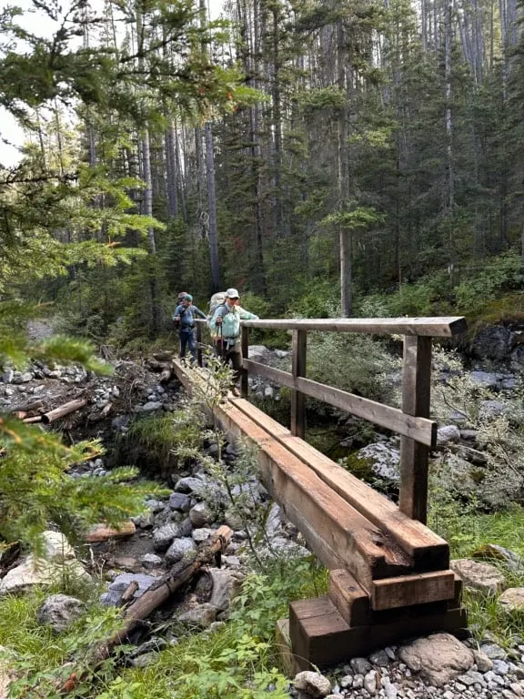 Two people cross a long, narrow bridge over Sunshine Creek in Banff National Park