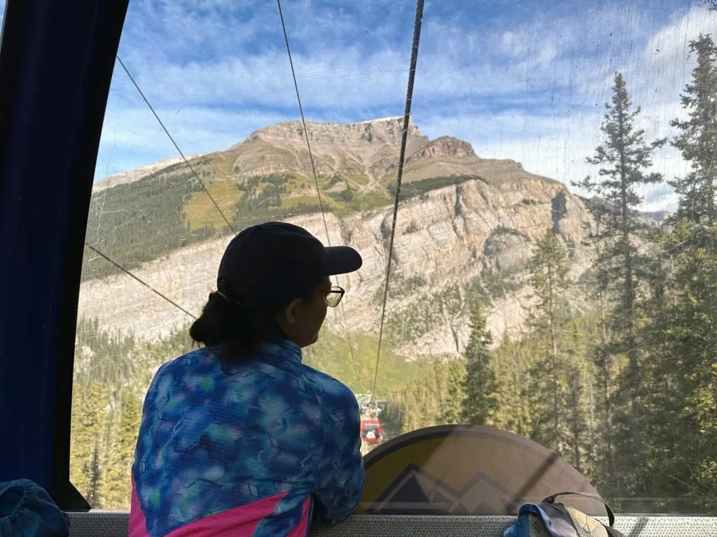 A woman looks out the window at the mountains from inside the Sunshine Village Gondola