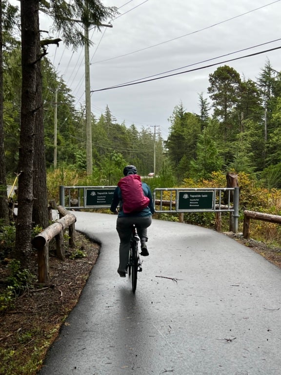 A woman wearing a pink backpack bikes on the ʔapsčiik t̓ašii bike path in Pacific Rim National Park