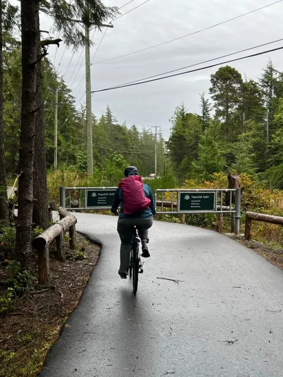 A woman wearing a pink backpack bikes on the ʔapsčiik t̓ašii bike path in Pacific Rim National Park