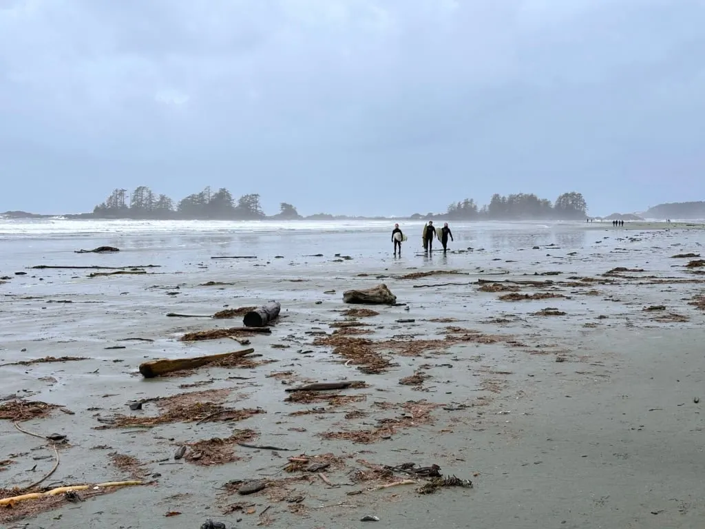 Surfers walk along the beach carrying surfboards at Chesterman Beach in Tofino