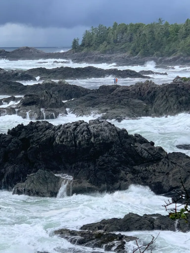 People stand on a rock surrounded by crashing waves as seen from the Wild Pacific Trail in Ucluelet