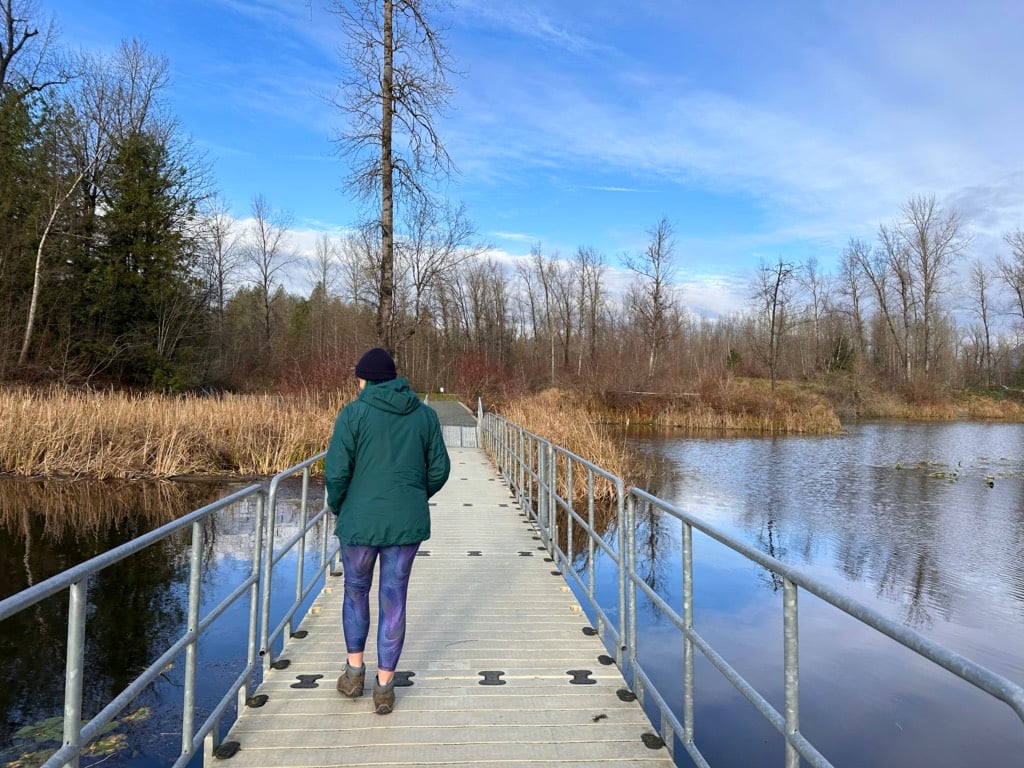 A woman in a green jacket walks along a floating walkway at Cheam Lake Wetlands