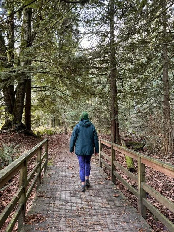 A woman in a green jacket walks over a wooden bridge in the forest on the Miami Bridges Trail in Harrison