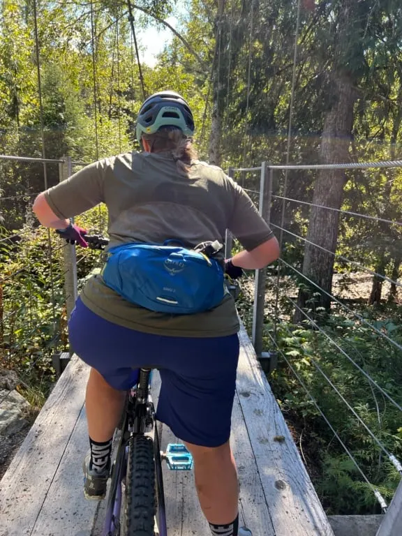 A woman wears a blue Osprey Savu 2 waist pack while mountain biking